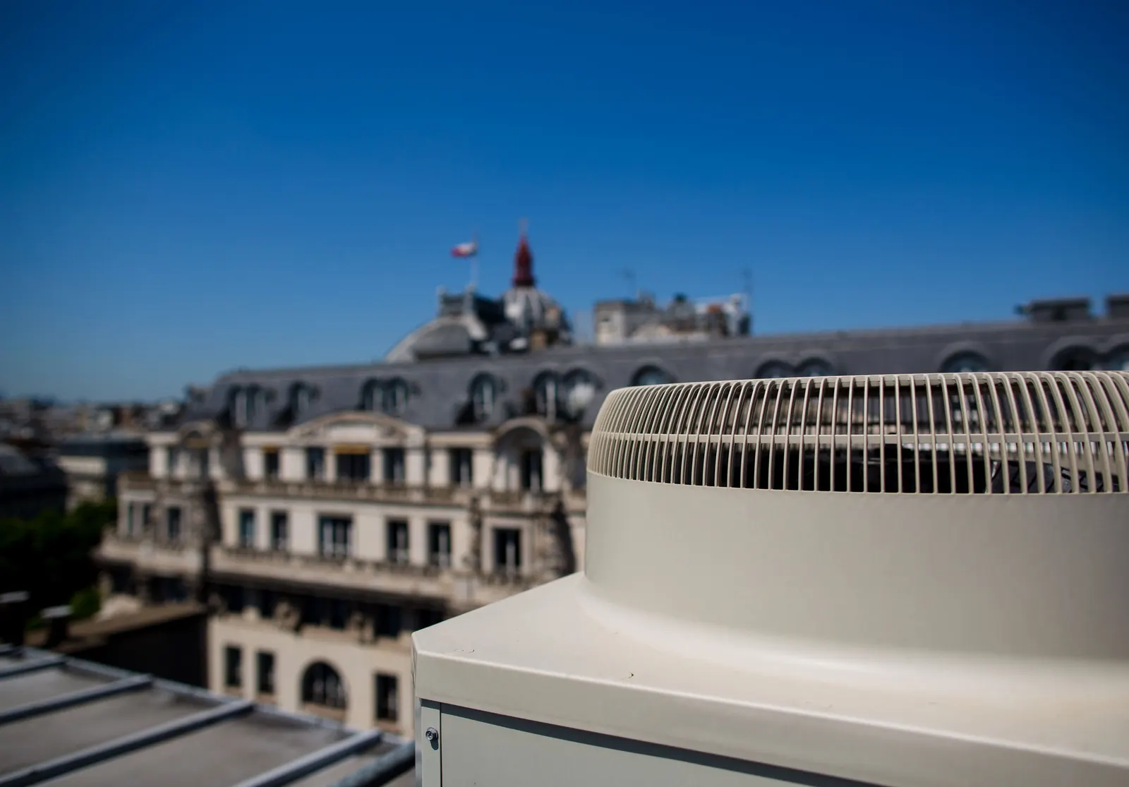 Unité extérieure de climatisation installée sur un toit, face à un immeuble parisien